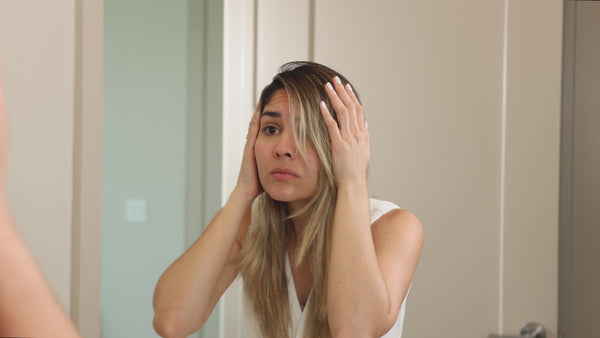Woman examining her hair in the mirror before applying Growth Essence Minoxidil Shampoo.